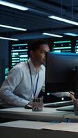 Vertical Management executive in data center ensuring system can handle networking tasks. Coworkers doing brainstorming in server room, tracking network traffic with PC, making improvements, camera B video