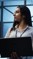 Vertical Admin in data center managing servers, operating systems and software programs. Tracking shot of woman in server hub ensuring networks are secure, up to date, and functioning properly, camera B video