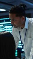 Vertical Team of admins in data center ensuring system can handle networking tasks. Teamworking colleagues in server room tracking network traffic with PC, making improvements, camera A video