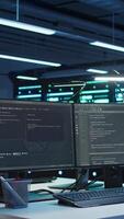 Vertical High tech data center with networking systems installed used for managing hardware. Code running on computer screens in technologically advanced server hub used for overseeing equipment, panning shot video