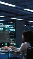 Vertical Person with paraplegia working in inclusive server hub workspace, typing on PC. Woman in wheelchair doing tasks in data center housing advanced data storage infrastructure, camera B video