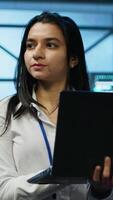 Vertical System administrator in data center monitoring security threats, implementing cybersecurity measures. Woman ensuring compliance with regulations to protect data center gear, camera A video