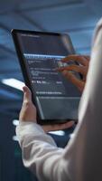 Vertical Data center software developer responsible for installation of networking equipment solving tasks on device. Close up of woman doing maintenance on server room infrastructure using tablet, camera B video