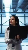 Vertical System administrator in data center monitoring security threats, implementing cybersecurity measures. Woman ensuring compliance with regulations to protect data center gear, camera B video
