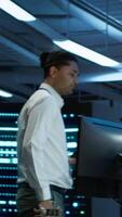 Vertical Team of programmers in high tech data center troubleshooting issues using tablet. Teamworking colleagues in server farm using device, establishing performance benchmarks, camera A video
