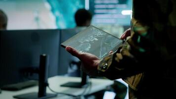 Military officer leads cybersecurity operations in a high tech operation room command post, ensuring data protection. Soldiers working with cctv surveillance systems, satellite imagery. Camera A. video