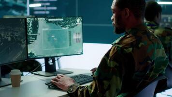 Team of military specialists overseeing surveillance activity by using a cctv footage and radar, pointing at a big screen and world map. High tech control center base of operations. Camera A. video