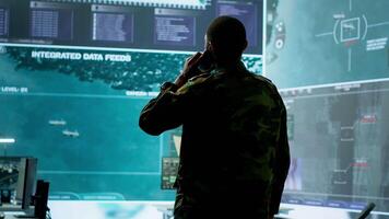 Military man answers phone call in a mission control center, working with advanced technology and satellite imagery to track potential threats and real time data. Intelligence activities. Camera A. video