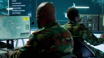 Military personnel in a base of operations using advanced computers and big screen, monitoring satellite systems to enhance security measures and process data. High tech army gear. Camera A. video