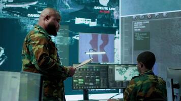 Military staff work in a high tech monitoring room command post, managing cybersecurity operations and surveillance systems. Soldier ensures data protection for national safety. Camera A. video