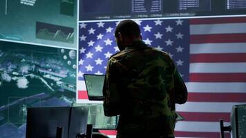 Professionals in US military uniforms operate computers and big screen, working on surveillance and intelligence to ensure national security from a high tech control center. Camera A. video