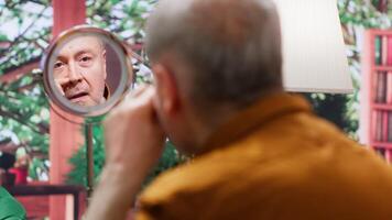 Old person applying rejuvenating lotion and UV protection cream to preserve his aging skin, looking in the mirror and doing daily routine for skincare. Elderly man using grooming products. Camera A. video