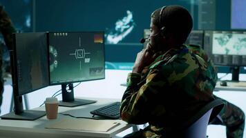 Army professional in uniform works in a mission control center, coordinating surveillance systems and processing intelligence data for operations. Ensuring strategic planning and defense. Camera A. video