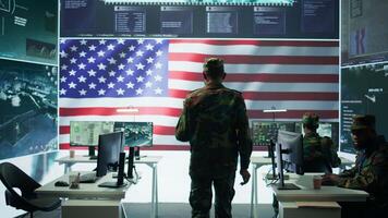 Military personnel in a base of operations using advanced computers and big screen, monitoring satellite systems to enhance security measures and process data. High tech army gear. Camera B. video