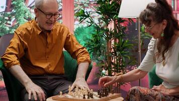 Elderly couple enjoying a chess game competition for leisure at home, showcasing companionship and intellectual hobbies. Man and woman relaxing with a board game strategy as a pastime. Camera A. video