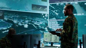 Military officers work in a high tech army control tower base, managing surveillance imagery from cctv satellite. Soldiers handle data protection to ensure national security. Camera A. video