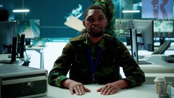 Military intelligence expert conducts a strategic teleconference connection in a modern command post, utilizing real time data on multiple screens for communication and decision making. Camera A. video