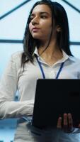 Vertical Admin in data center managing servers, operating systems and software programs. Tracking shot of woman in server hub ensuring networks are secure, up to date, and functioning properly, camera A video