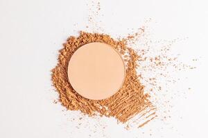 A round block of compact powder in a natural tone stands on a sample of loose powder in a dark tone. top view.textures of powders. layout. photo