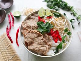 A Bowl Pho Bo traditional Soup with beef, rice noodles, ginger, lime, chili pepper in bowl. Close up. Vietnamese cuisine served on black background photo