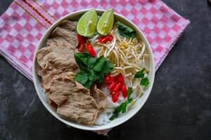 A Bowl Pho Bo traditional Soup with beef, rice noodles, ginger, lime, chili pepper in bowl. Close up. Vietnamese cuisine served on black background photo