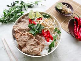 A Bowl Pho Bo traditional Soup with beef, rice noodles, ginger, lime, chili pepper in bowl. Close up. Vietnamese cuisine served on black background photo