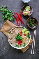A Bowl Pho Bo traditional Soup with beef, rice noodles, ginger, lime, chili pepper in bowl. Close up. Vietnamese cuisine served on black background photo