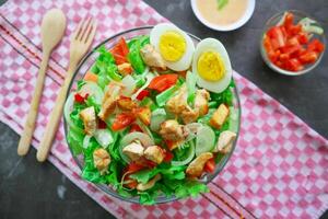 A cesar salad bowl filled with lettuce, tomatoes, egg and chicken. The salad is served in a clear glass bowl photo