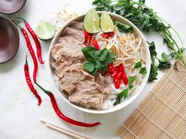 A Bowl Pho Bo traditional Soup with beef, rice noodles, ginger, lime, chili pepper in bowl. Close up. Vietnamese cuisine served on black background photo