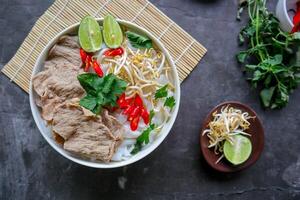 A Bowl Pho Bo traditional Soup with beef, rice noodles, ginger, lime, chili pepper in bowl. Close up. Vietnamese cuisine served on black background photo