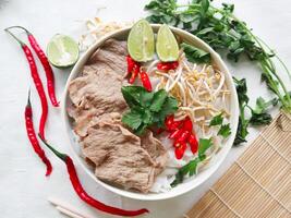 A Bowl Pho Bo traditional Soup with beef, rice noodles, ginger, lime, chili pepper in bowl. Close up. Vietnamese cuisine served on black background photo