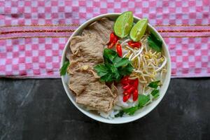 A Bowl Pho Bo traditional Soup with beef, rice noodles, ginger, lime, chili pepper in bowl. Close up. Vietnamese cuisine served on black background photo
