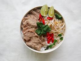 A Bowl Pho Bo traditional Soup with beef, rice noodles, ginger, lime, chili pepper in bowl. Close up. Vietnamese cuisine served on black background photo