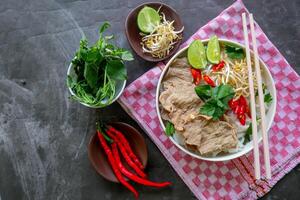 A Bowl Pho Bo traditional Soup with beef, rice noodles, ginger, lime, chili pepper in bowl. Close up. Vietnamese cuisine served on black background photo