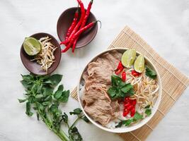 A Bowl Pho Bo traditional Soup with beef, rice noodles, ginger, lime, chili pepper in bowl. Close up. Vietnamese cuisine served on black background photo