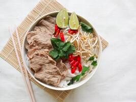 A Bowl Pho Bo traditional Soup with beef, rice noodles, ginger, lime, chili pepper in bowl. Close up. Vietnamese cuisine served on black background photo