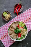 A Bowl Pho Bo traditional Soup with beef, rice noodles, ginger, lime, chili pepper in bowl. Close up. Vietnamese cuisine served on black background photo