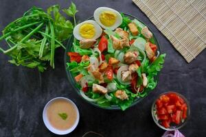 A cesar salad bowl filled with lettuce, tomatoes, egg and chicken. The salad is served in a clear glass bowl photo