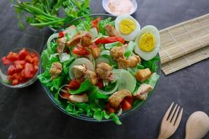A cesar salad bowl filled with lettuce, tomatoes, egg and chicken. The salad is served in a clear glass bowl photo