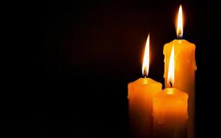 yellow burning candles with dripping wax close-up on a black background with space for text photo