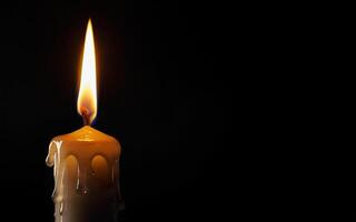 burning yellow candle and dripping wax on a black background with space for text photo