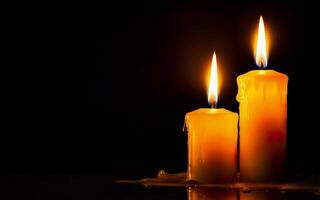 yellow burning candles with dripping wax on a black background with space for text photo