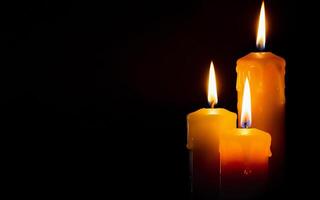 three yellow burning wax candles on a black background with space for text photo