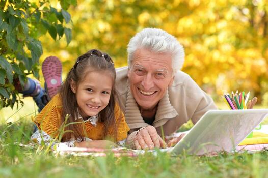 abuelo y nieta dibujo y utilizando ordenador portátil en otoño parque foto