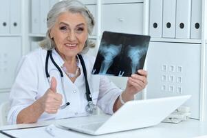 Portrait of elderly woman doctor sitting at table and looking at x-ray photo