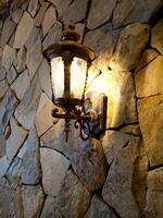 Lantern with flame in retro style on the background of a stone wall of an ancient house. photo