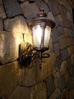 Lantern with flame in retro style on the background of a stone wall of an ancient house. photo