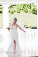 A bride is posing for a picture with a veil and a bouquet of flowers. Concept of elegance and romance, as the bride is dressed in a white gown and is surrounded by a beautiful outdoor setting photo