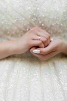 A woman is wearing a white dress and holding her hands together. She is wearing a gold wedding ring on her left hand photo