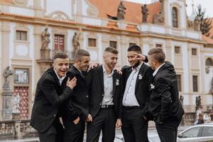 A group of men in suits are posing for a photo in front of a building. Scene is lighthearted and fun, as the men are smiling and laughing together
